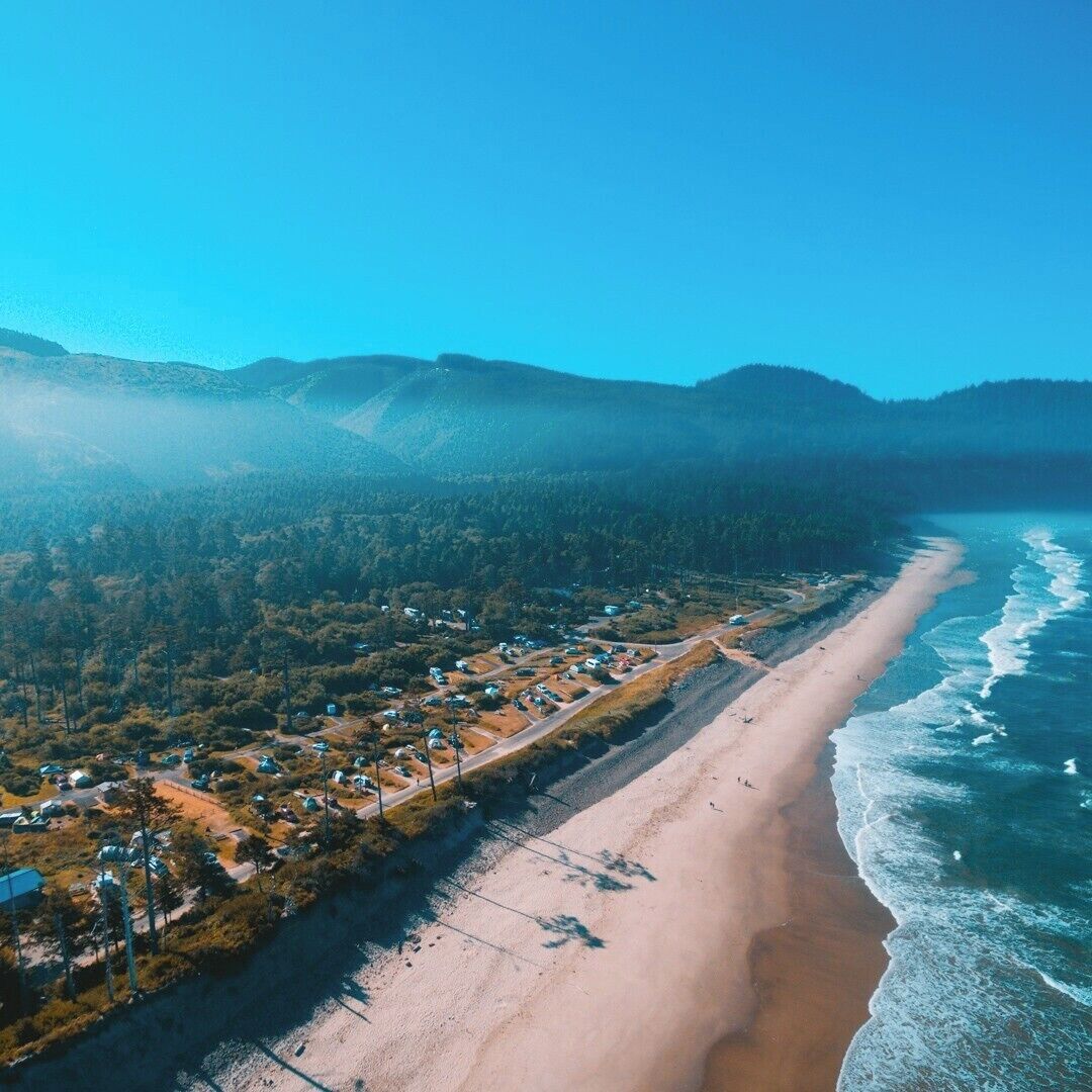 A coastal town with a beach, houses, and forested hills.