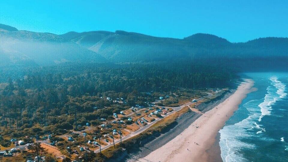A coastal town with a beach, houses, and forested hills.