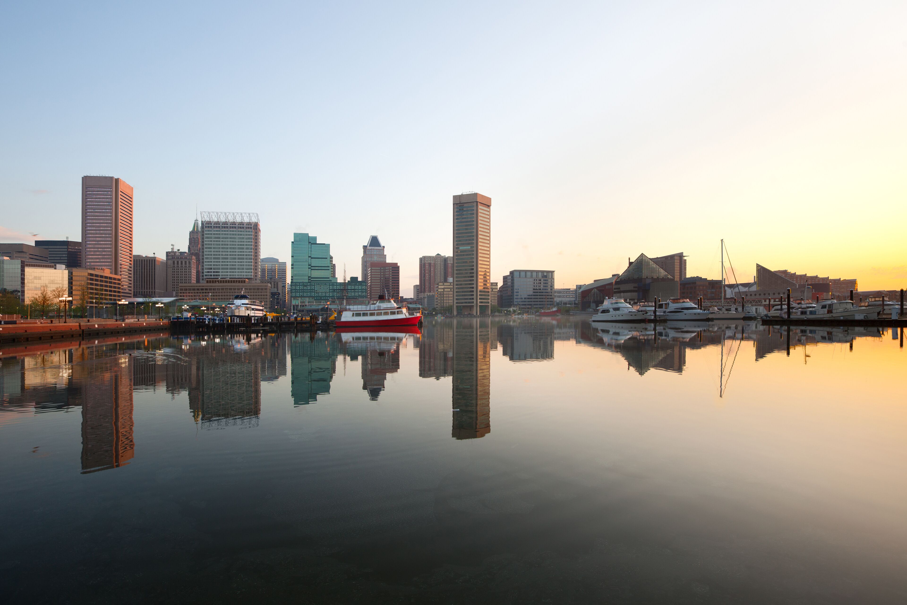 A city skyline reflected in calm water with a red and white boat docked at the pier.