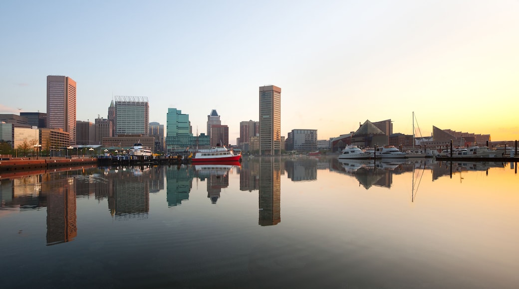 A city skyline reflected in calm water with a red and white boat docked at the pier.