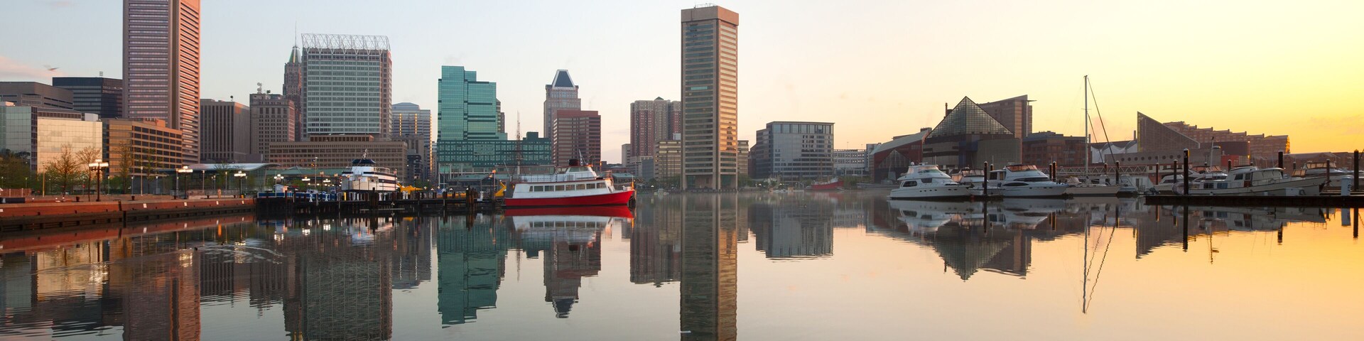Un horizonte urbano reflejado en agua tranquila con una embarcación roja y blanca amarrada al muelle.