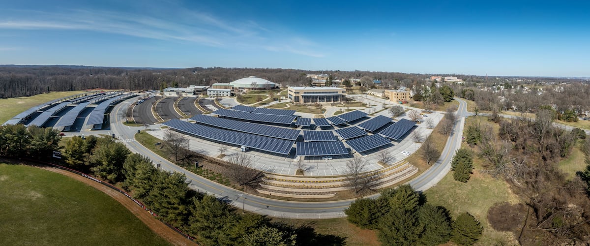 A solar farm with multiple rows of solar panels, surrounded by roads and buildings.