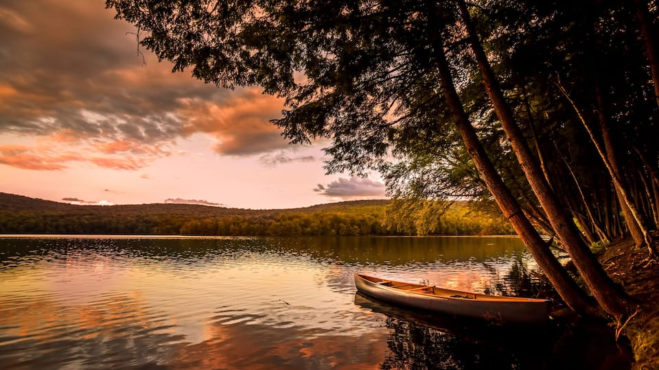 Canoe on the lake at sunset. Warm sunset colors spill over Mongaup Pond, the largest lake in the Catskills. One of the most popular summer vacation and camping destination in New York