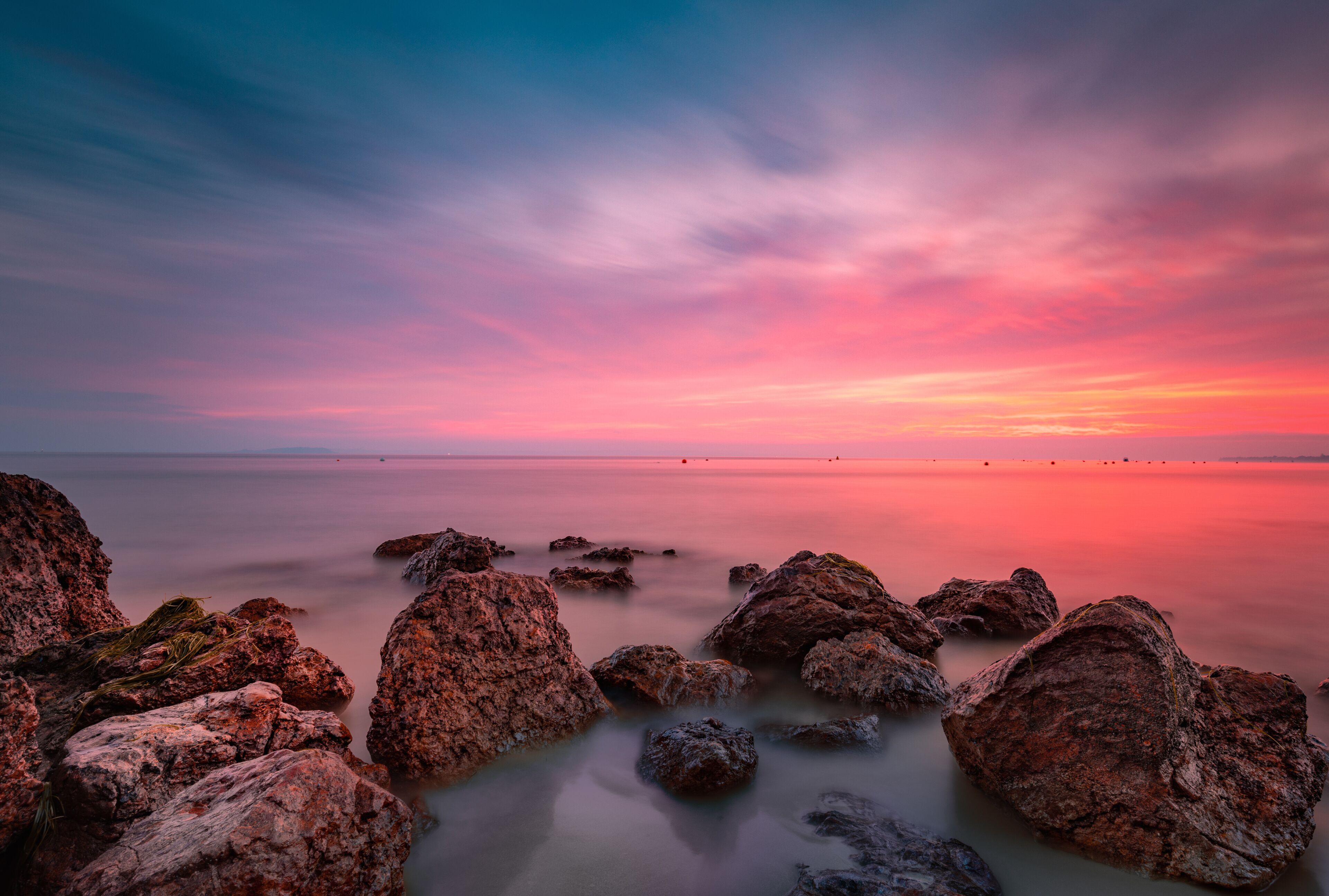 A coastal landscape with large rocks and a calm sea during sunset.