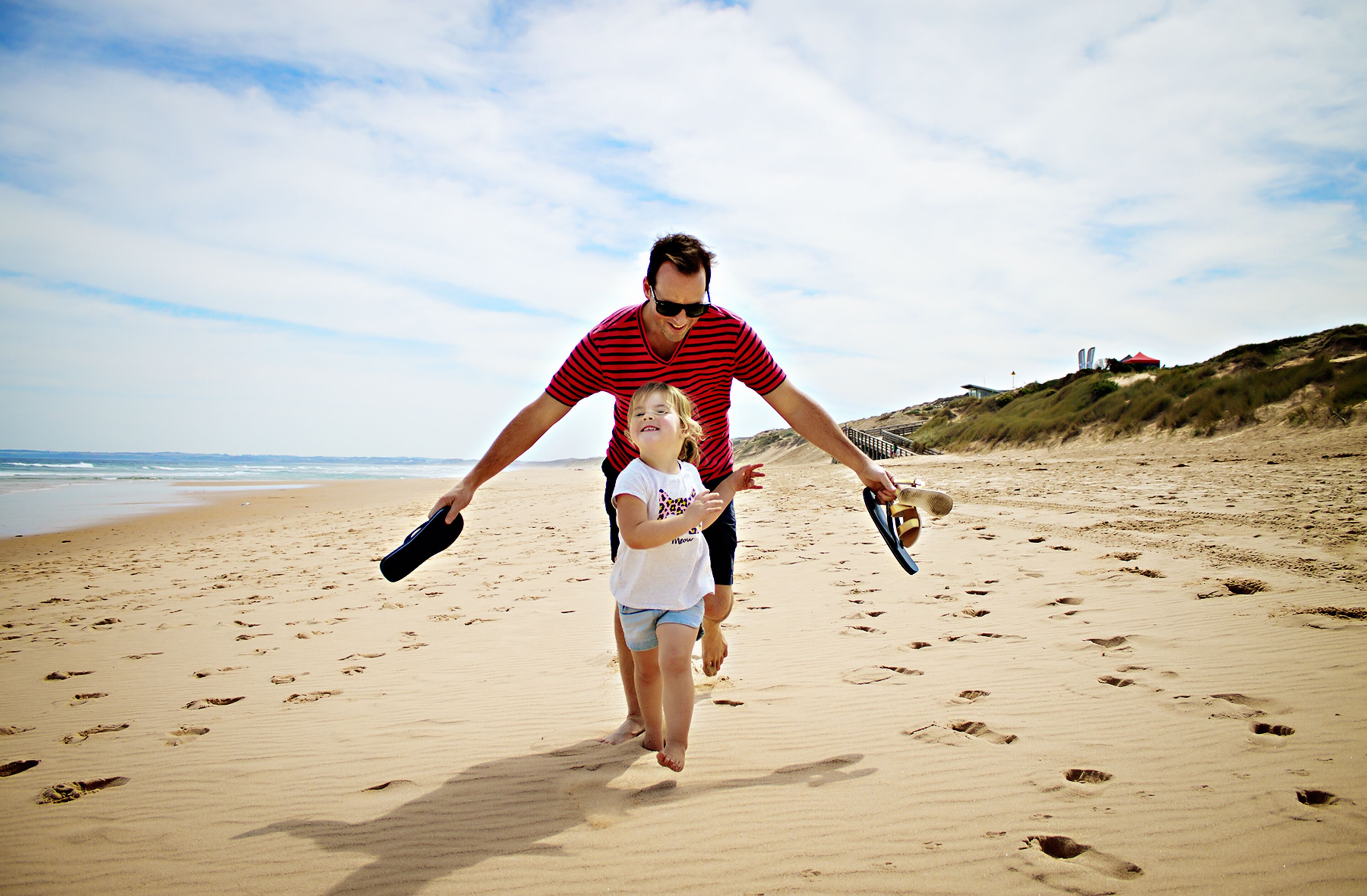 A sandy beach with footprints, a person in a striped shirt, and a child in a white shirt.