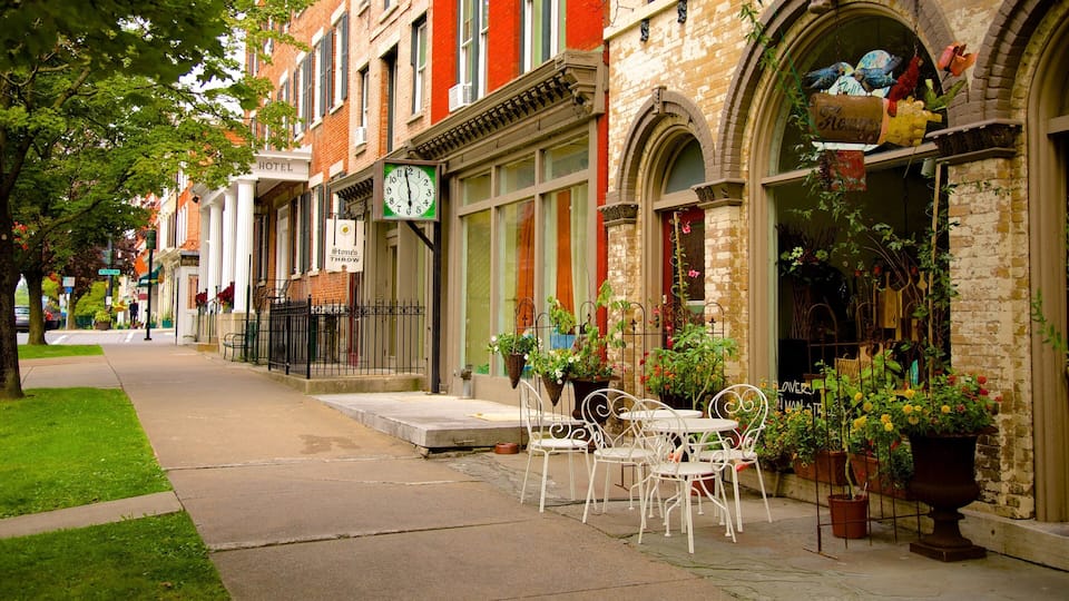 A street with a row of brick buildings, a clock, and outdoor seating with potted plants.