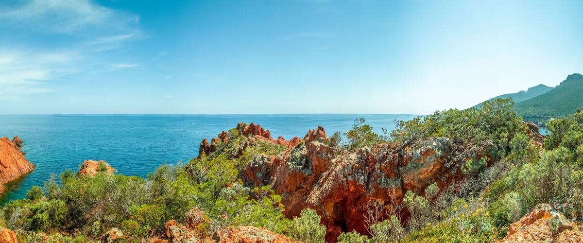 A coastal landscape with red cliffs, green vegetation, and a clear blue sea.
