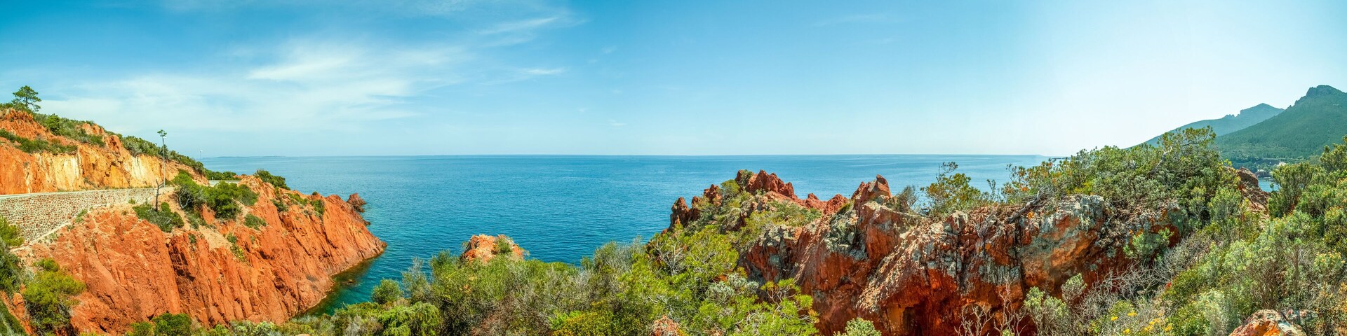 A coastal landscape with red cliffs, green vegetation, and a clear blue sea.