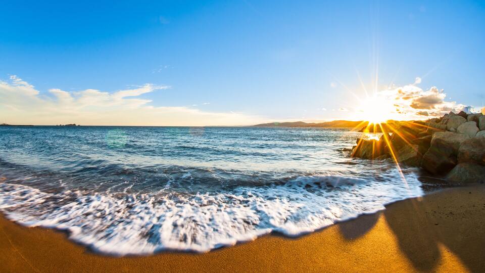 A beach with waves, a clear sky, and the sun setting over the horizon.