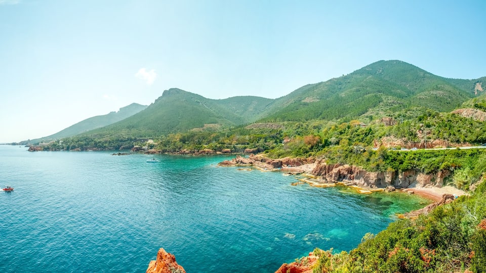 A coastal landscape with a clear blue sea, rocky cliffs, and green hills.