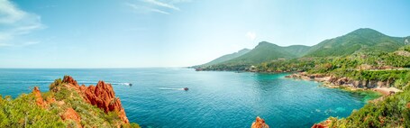 Un paysage côtier caractérisé par une mer bleue et limpide, des falaises rocheuses et des collines verdoyantes.