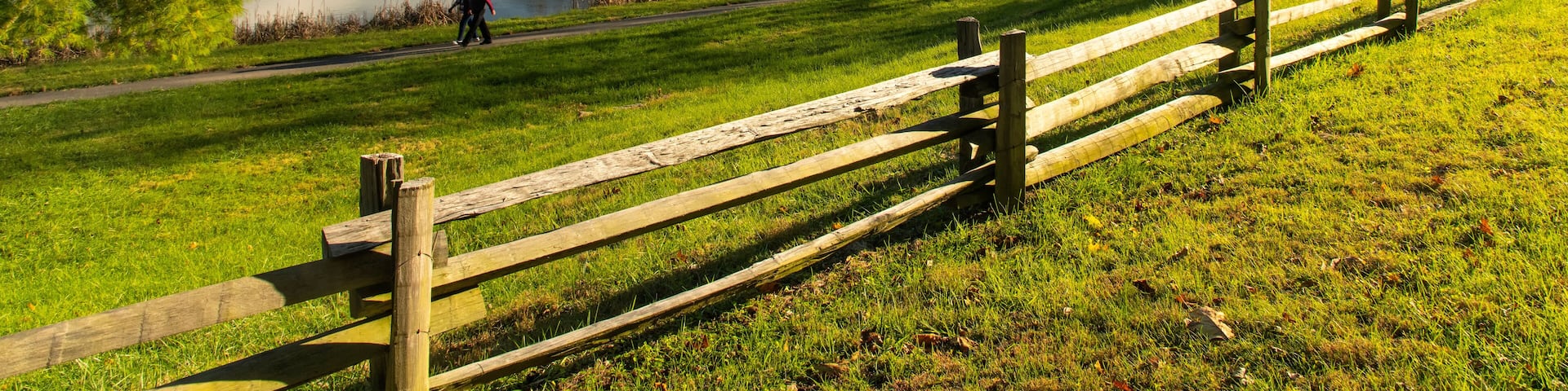 A lake, a wooden fence, a hilly landscape, and a person walking.