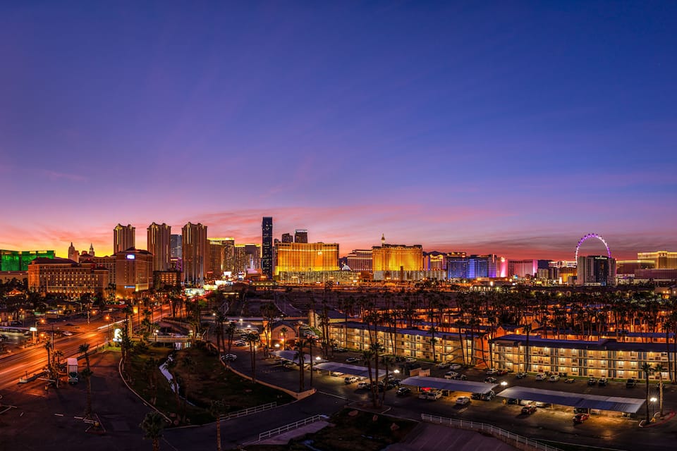 A cityscape at dusk with illuminated buildings and a prominent Ferris wheel.