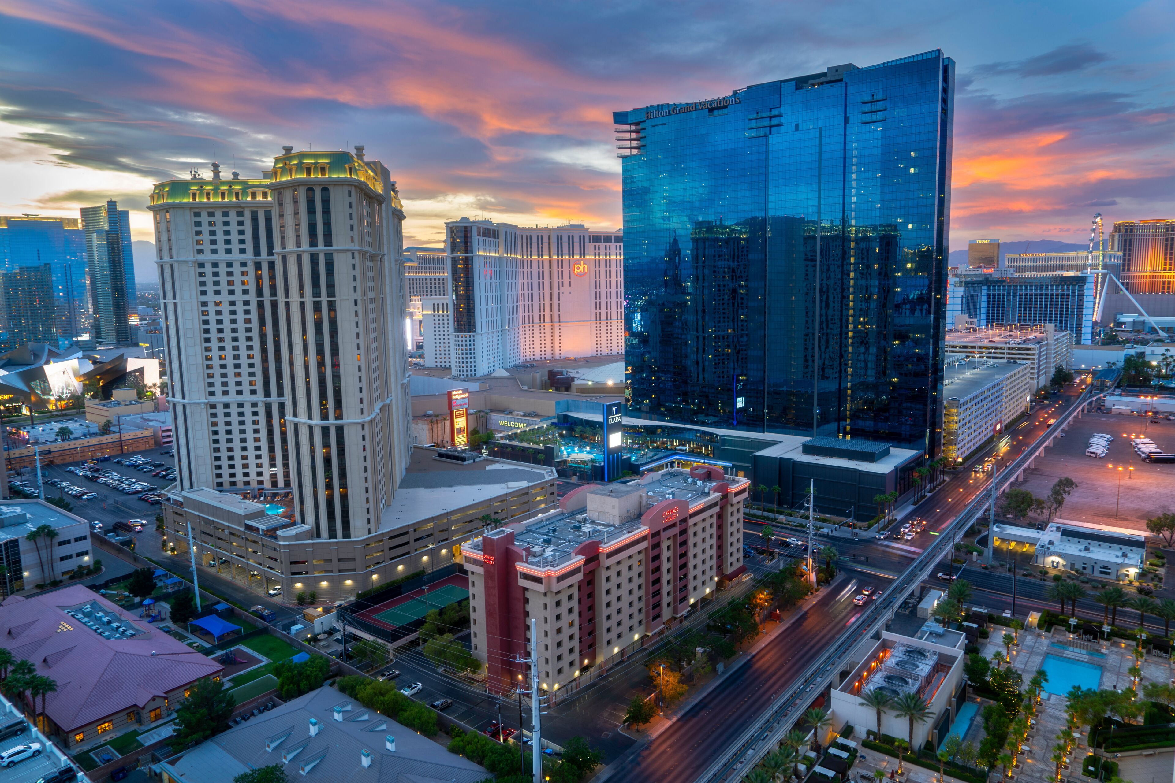 Aerial view of a modern glass hotel and casino in Las Vegas, Nevada at dusk with a colorful sunset and monorail