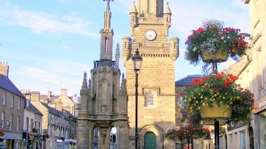 A historic stone tower with a clock, a street with buildings, and hanging flower baskets.