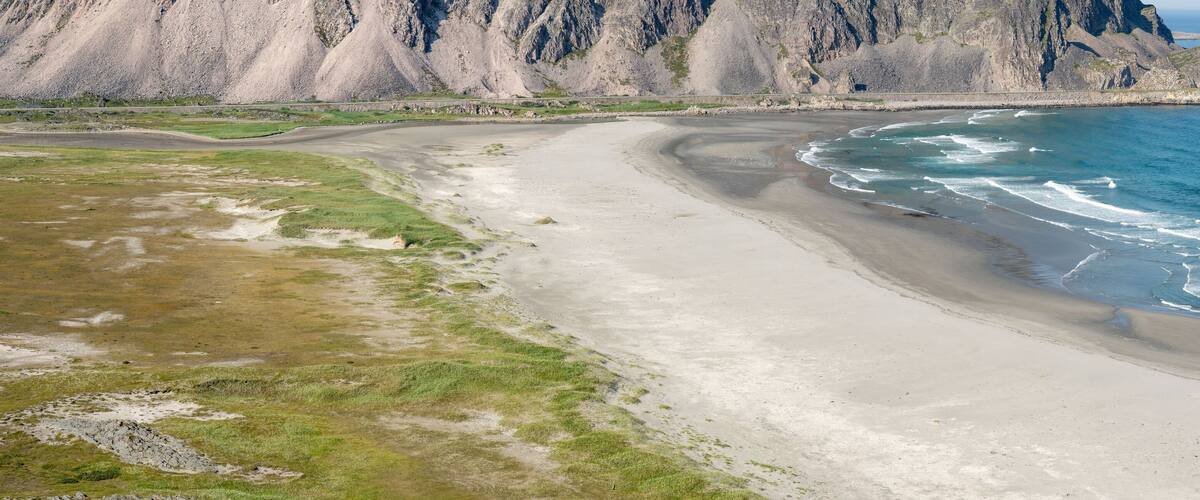 A coastal landscape with a sandy beach, rocky cliffs, and a clear view of the ocean.