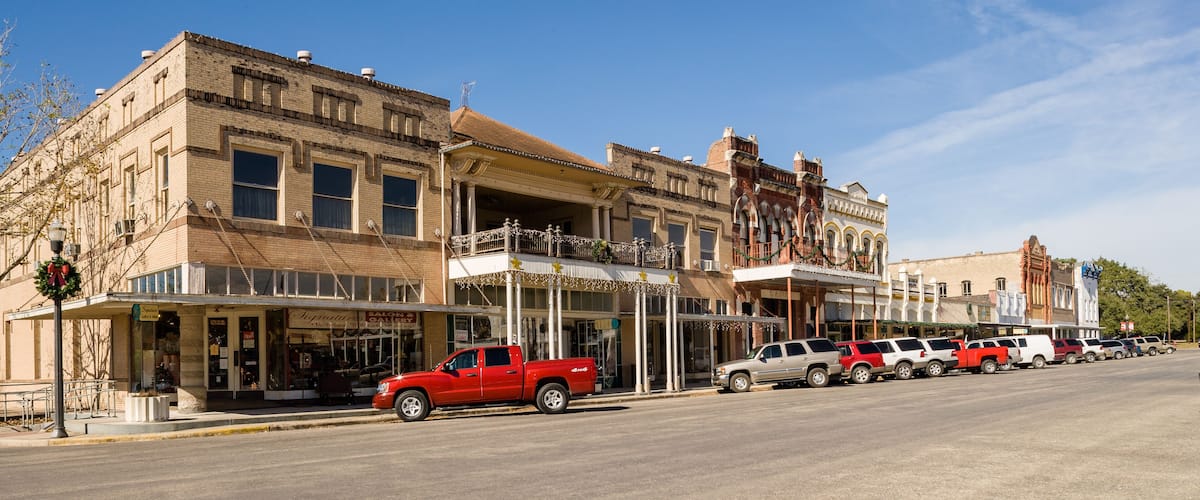 A street lined with historic buildings, a red truck parked on the side, and a row of parked cars.