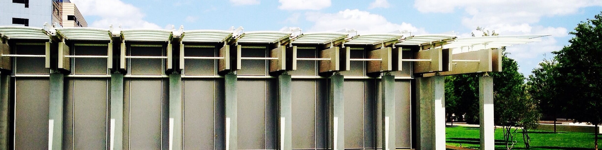 Un edificio moderno con techo plano y múltiples columnas, frente a un cielo azul despejado y césped verde.