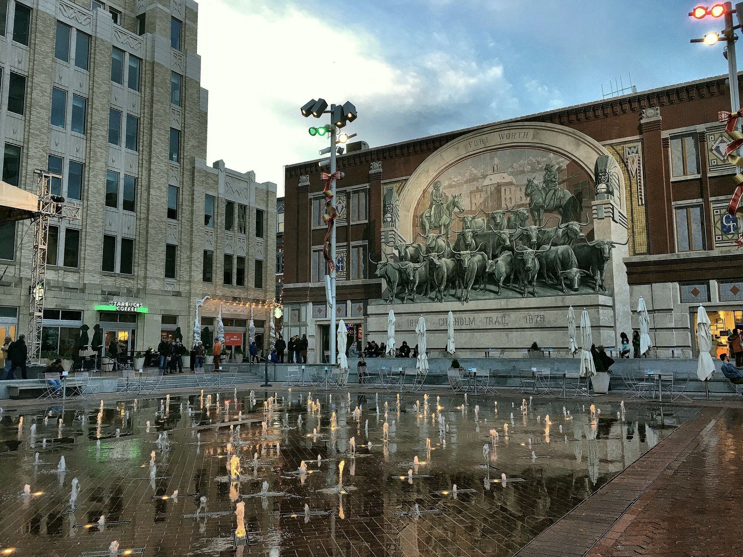 Una plaza urbana con una fuente, un mural de toros y un Starbucks.