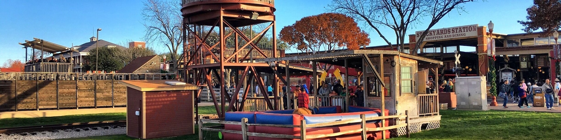 Una estación de tren antigua con una torre de agua de madera, mesas de picnic y un pequeño edificio con el rótulo 'Stockyards Station'.