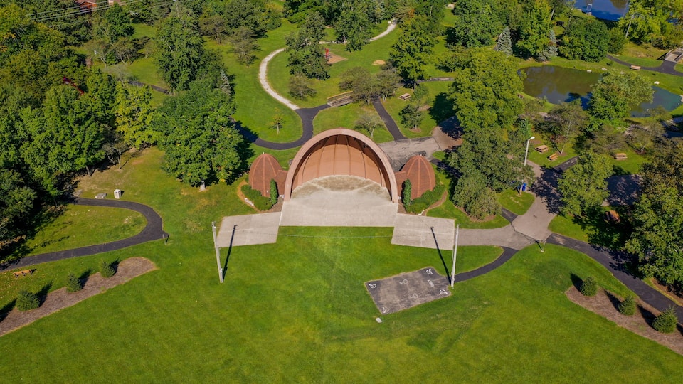 An aerial view of a park with a central dome structure, winding pathways, and a pond.