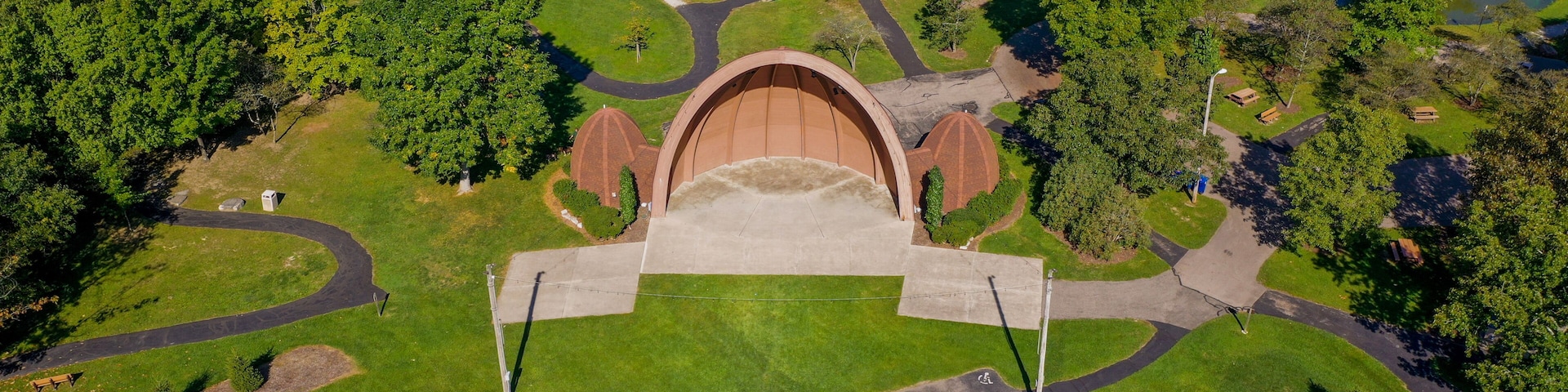 An aerial view of a park with a central dome structure, winding pathways, and a pond.