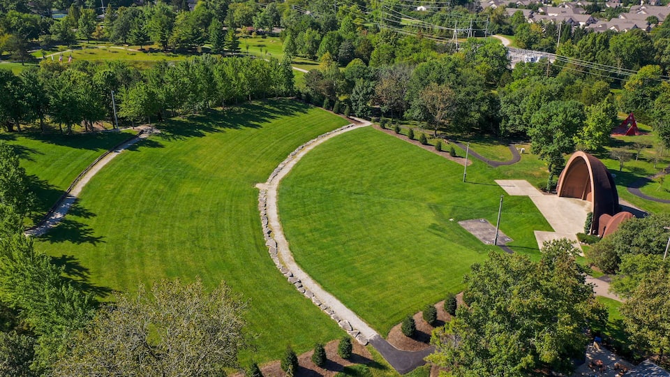 A well-maintained park with a curved lawn, a stone pathway, and a distinctive red arch structure.