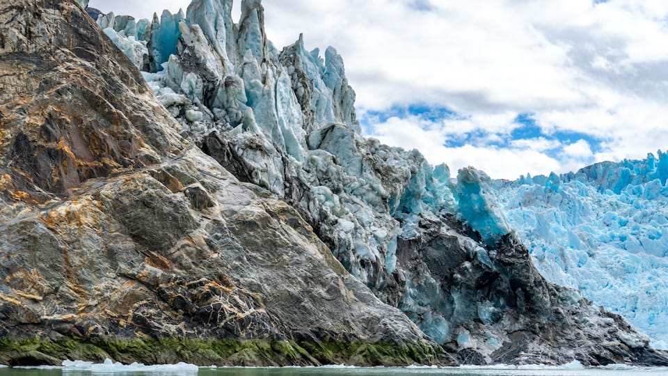 A glacier with sharp ice formations and a rocky foreground.