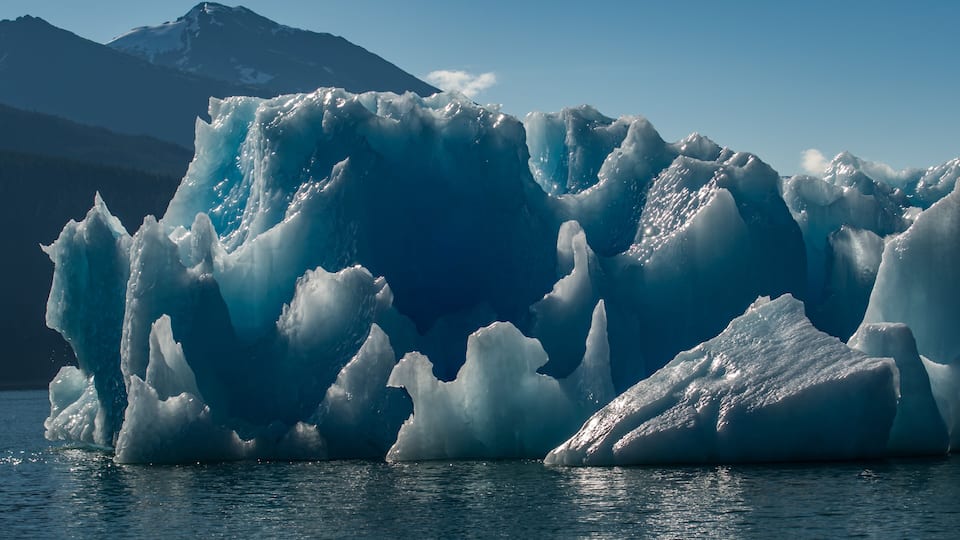 A large iceberg with sharp edges and a mountain in the background.