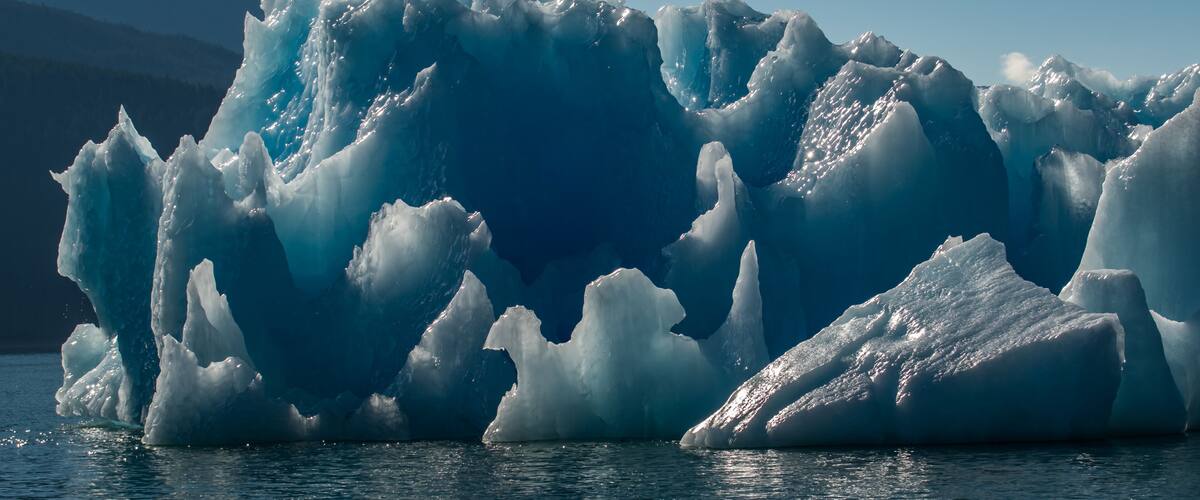 A large iceberg with sharp edges and a mountain in the background.