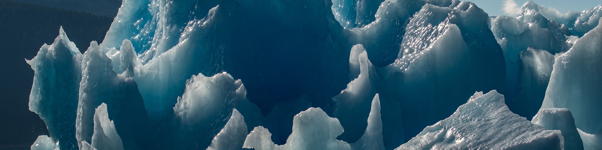 A large iceberg with sharp edges and a mountain in the background.