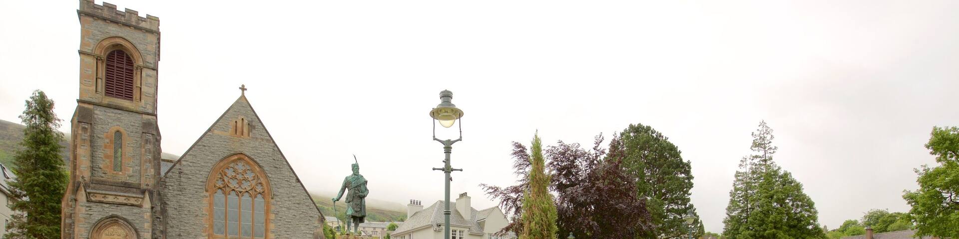 A church with a tall tower, a statue, and a well-maintained garden.