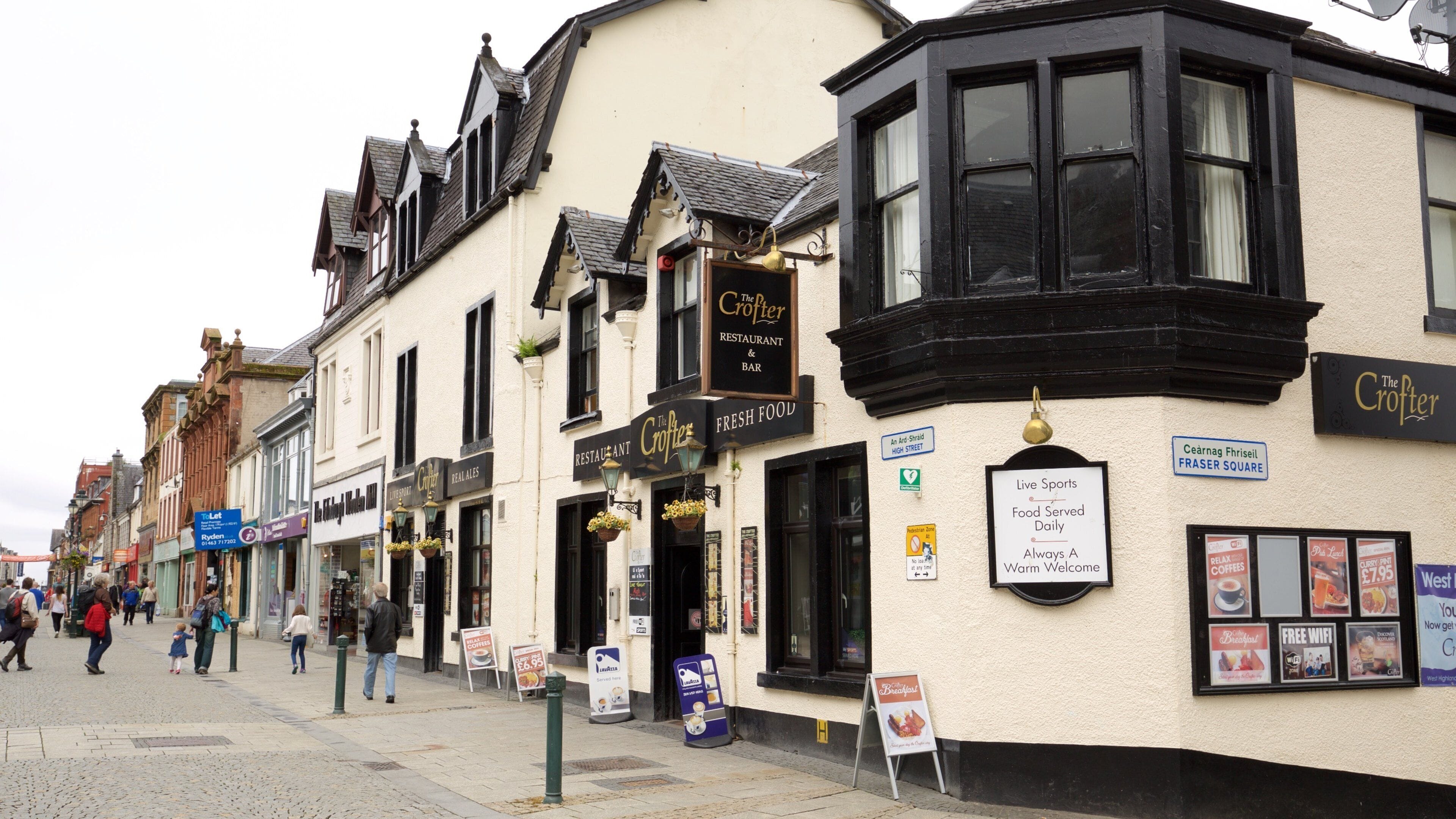 Une rue bordée d’immeubles, dont le restaurant-bar The Crofter, et où l’on peut voir des panneaux indiquant la diffusion d’événements sportifs en direct et la présence d’une connexion Wi-Fi gratuite.