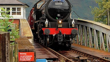 A steam locomotive on a railway track with a warning sign and a mountainous landscape in the background.