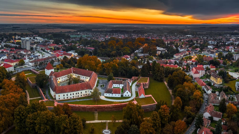 Sarvar, Hungary - Aerial panoramic view of the Castle of Sarvar (Nadasdy castle) with Sarvar Arboretum, a beautiful dramatic sunrise and rain clouds at background on a calm autumn morning