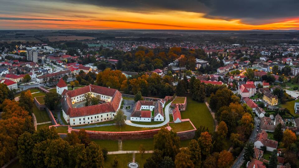 An aerial view of a town with a prominent historical fort surrounded by residential buildings and autumn foliage.