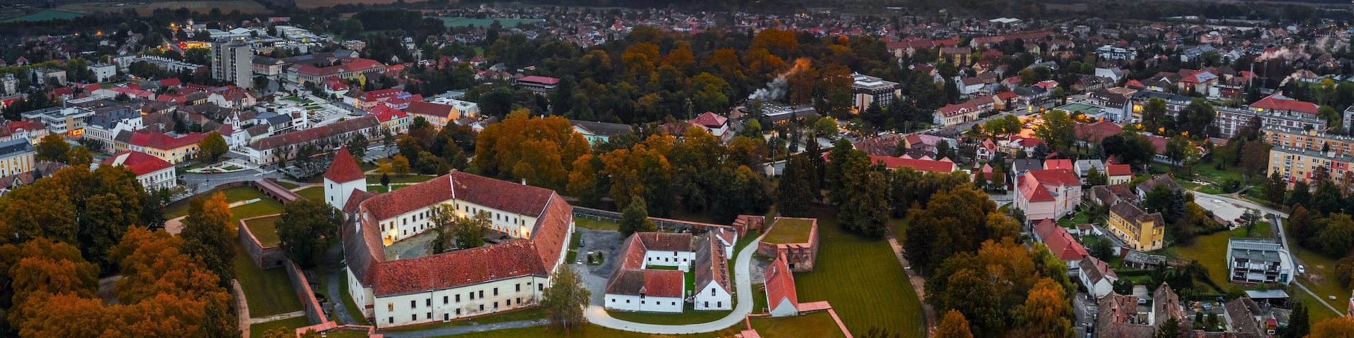 Sarvar, Hungary - Aerial panoramic view of the Castle of Sarvar (Nadasdy castle) with Sarvar Arboretum, a beautiful dramatic sunrise and rain clouds at background on a calm autumn morning