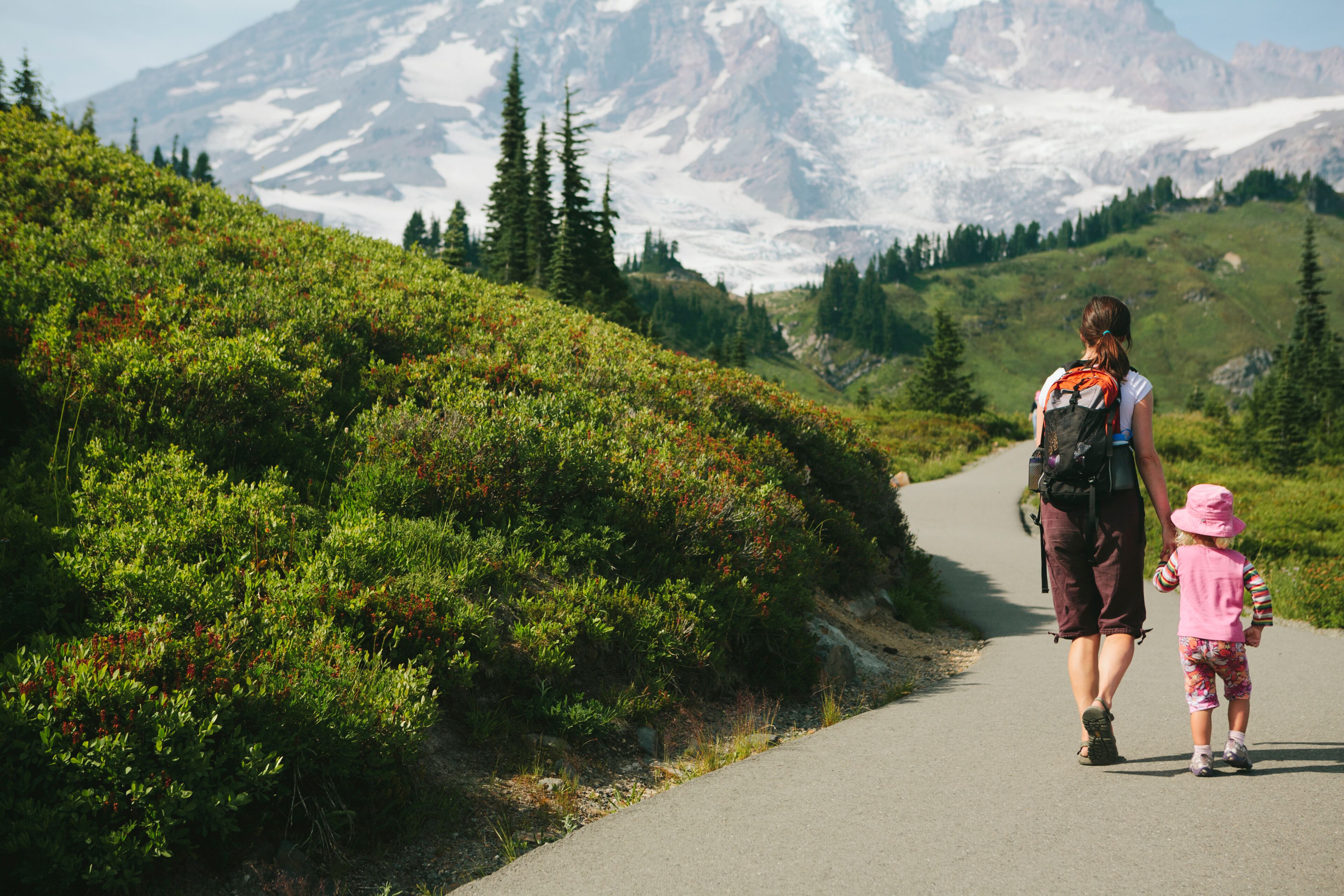 Mother and young daughter holding hands and walking on trail, Mt. Rainier in distance