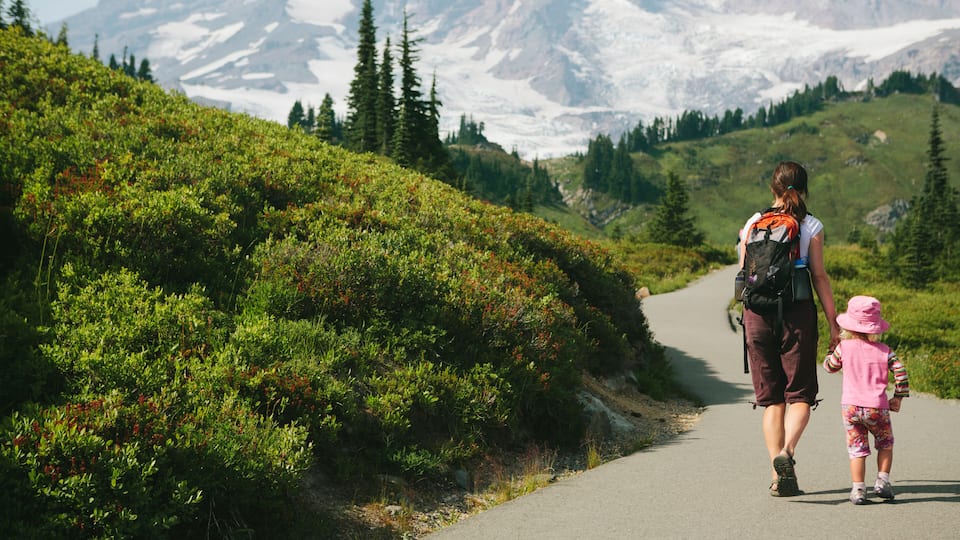 Mother and young daughter holding hands and walking on trail, Mt. Rainier in distance