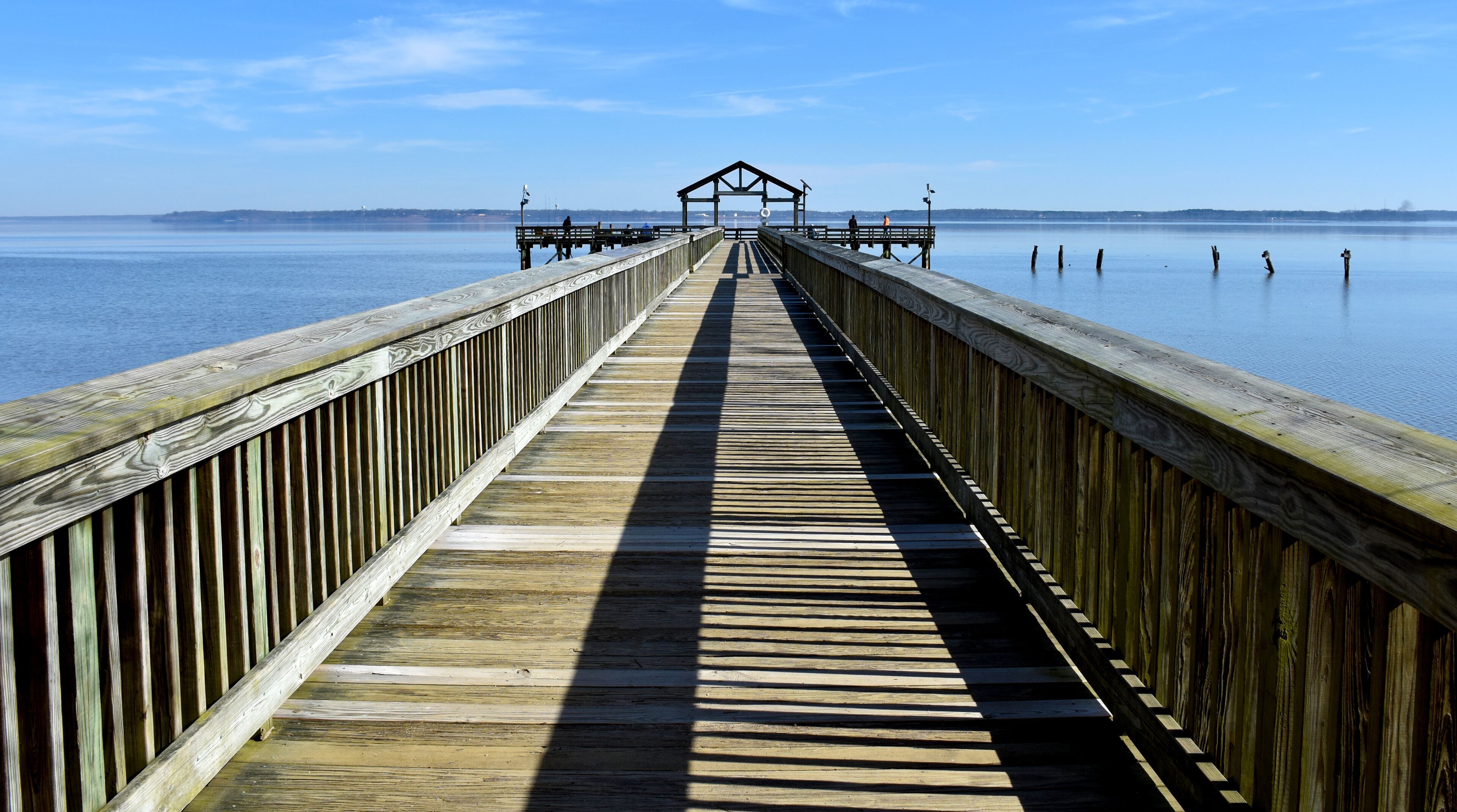 A wooden pier extending into calm water with a clear sky.