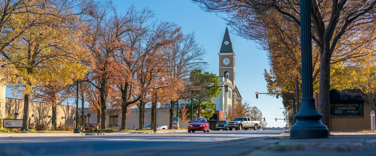 A street with autumn trees, a clock tower, and parked cars.