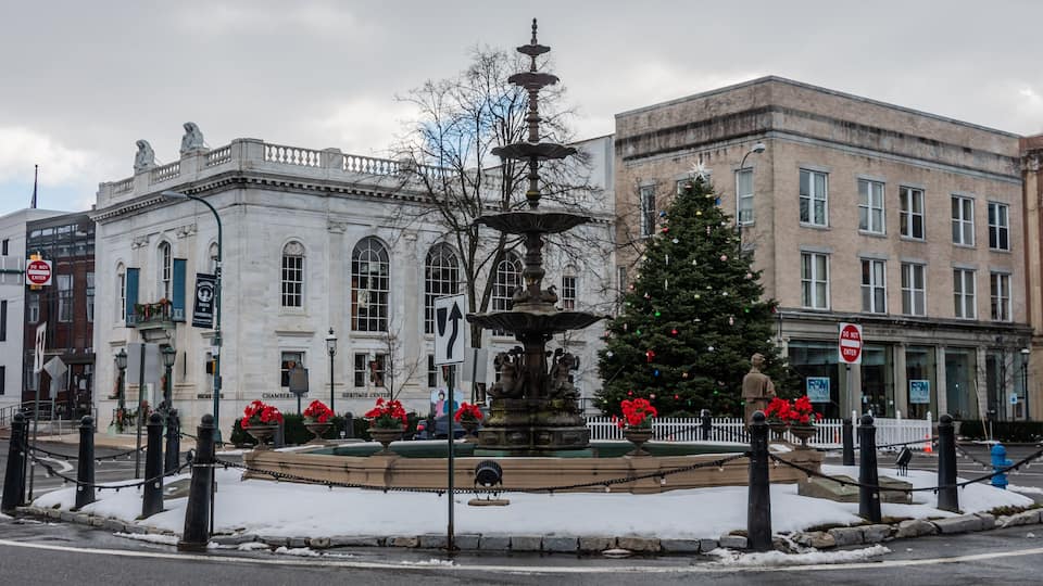 A public square with a fountain, a Christmas tree, and historic buildings.
