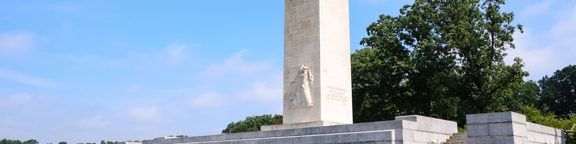 A tall monument with a statue on top, surrounded by grass and trees.