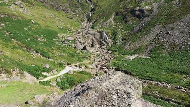 A mountainous landscape with a rocky path, green vegetation, and a waterfall.