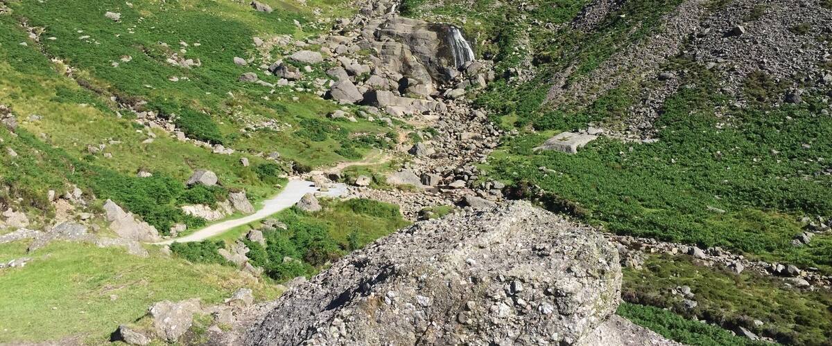 A mountainous landscape with a rocky path, green vegetation, and a waterfall.