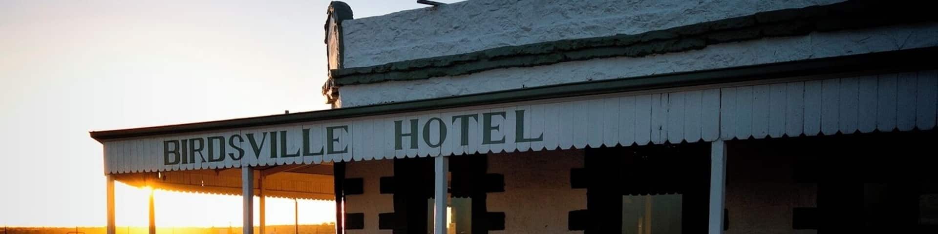 A building labeled 'Birdsville Hotel' with a distinctive facade and a bench in front.