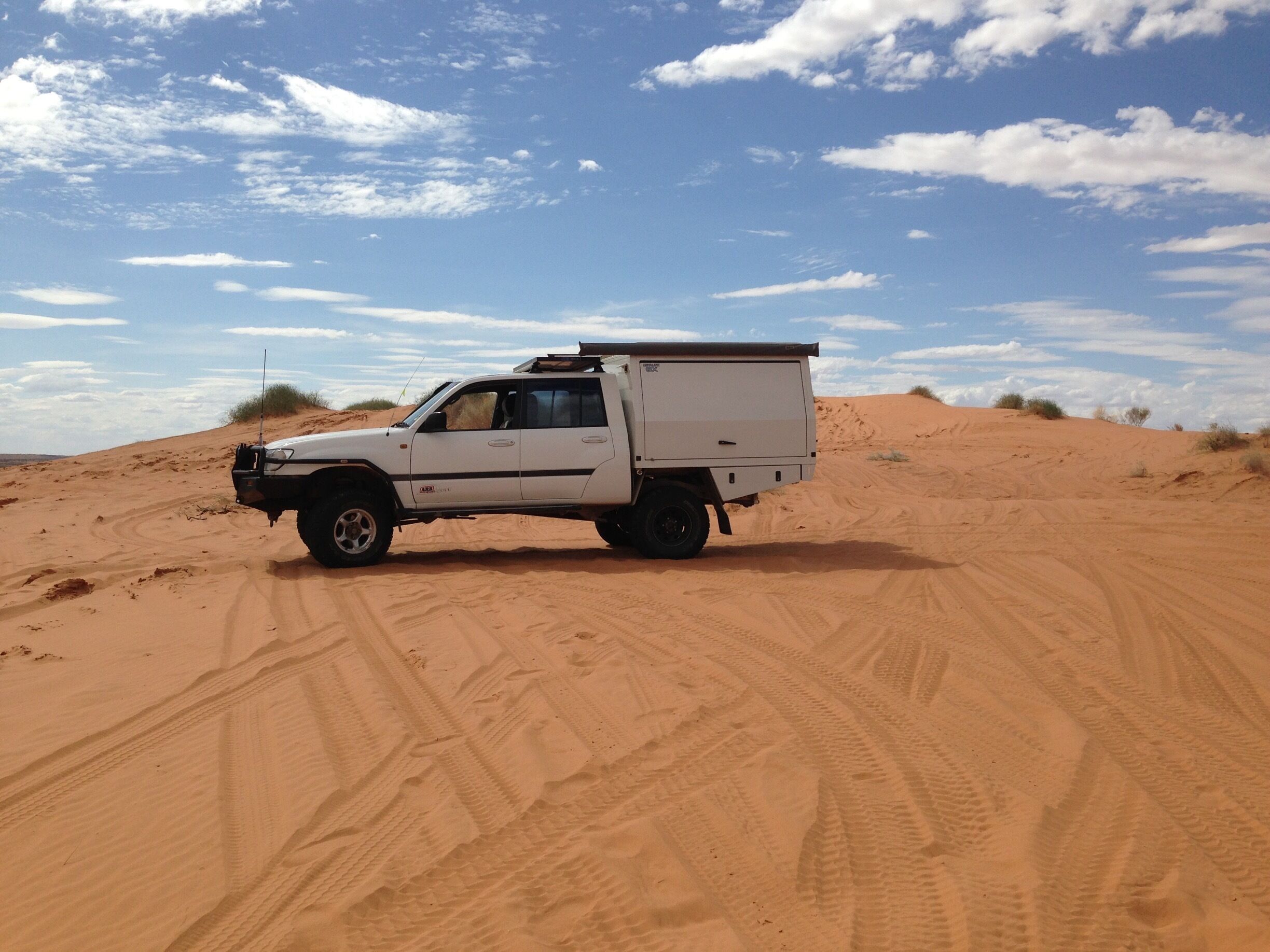 A white pickup truck with a cargo bed parked on a sandy dune.