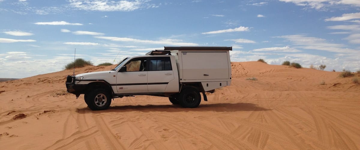 A white pickup truck with a cargo bed parked on a sandy dune.