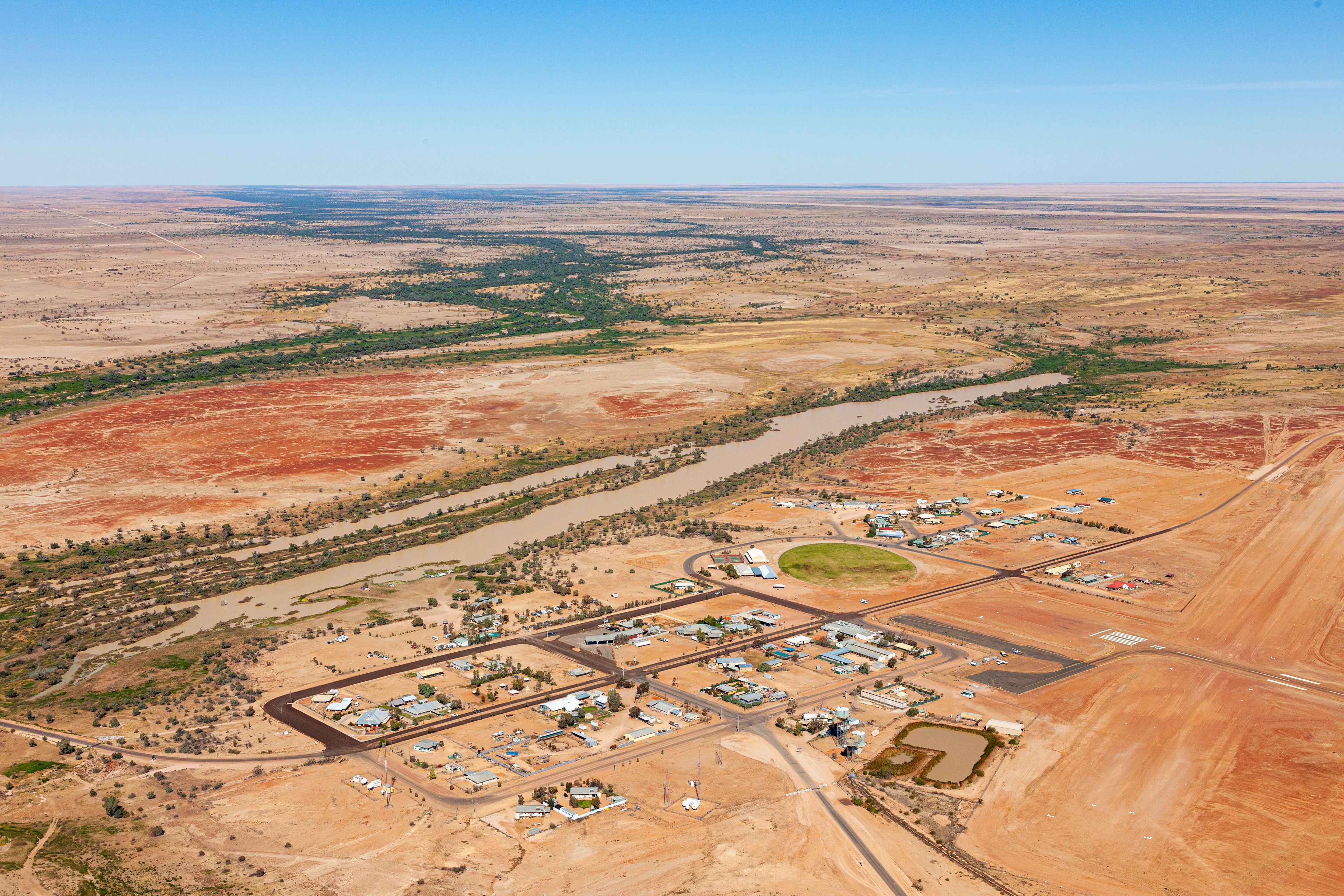 An aerial view of a town with a river running through it, surrounded by arid landscape.