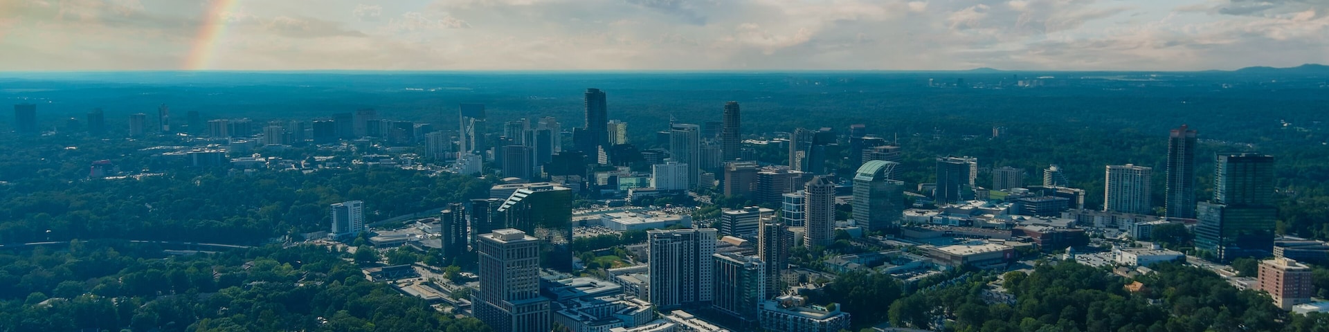a stunning aerial shot of vast miles of lush green trees with a view of the buildings nestled in the trees and shot of the cityscape with powerful clouds at Lennox Park in Brookhaven Georgia USA